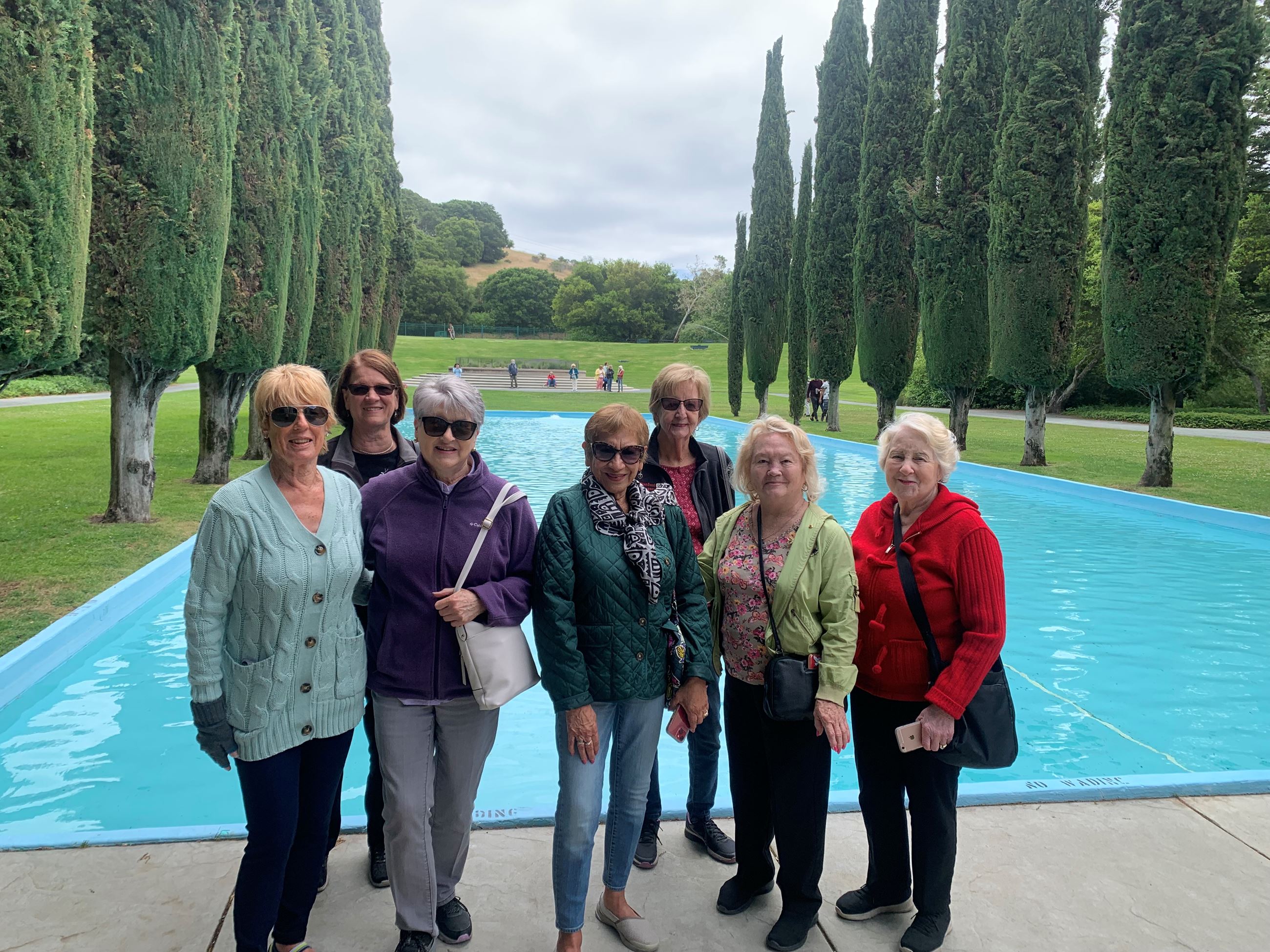 Seven women standing near body of water with cypress trees